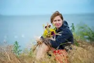 Smiling woman holding wildflowers by the seaside, enjoying summer outdoors.